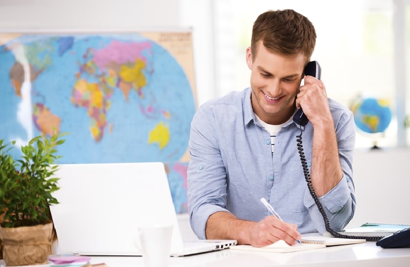 Mann am Telefon in einem Reisebüro schreibt sich etwas auf